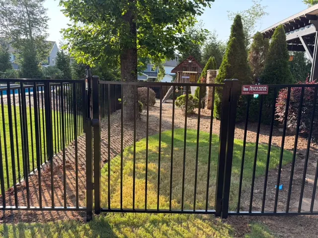 Black aluminum pool fence with a self-latching gate beside a play area, installed by Superior Fence & Rail of Raleigh