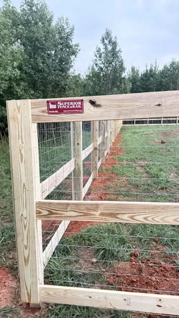 Wood-frame field fence with wire mesh with a wood-frame gate on an open pasture, installed by Superior Fence & Rail of Raleigh