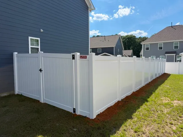 White vinyl privacy fence with a gate alongside a new-construction home, installed by Superior Fence & Rail of Raleigh