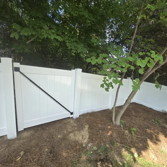 White vinyl privacy fence with a braced gate under mature trees, installed by Superior Fence & Rail of Raleigh