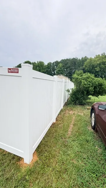 White vinyl privacy fence running along an open rural lot, installed by Superior Fence & Rail of Raleigh