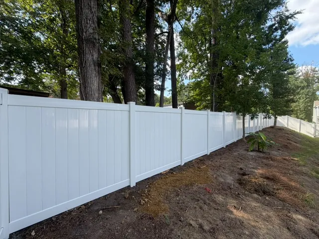 White vinyl privacy fence following grade beside a wooded lot, installed by Superior Fence & Rail of Raleigh