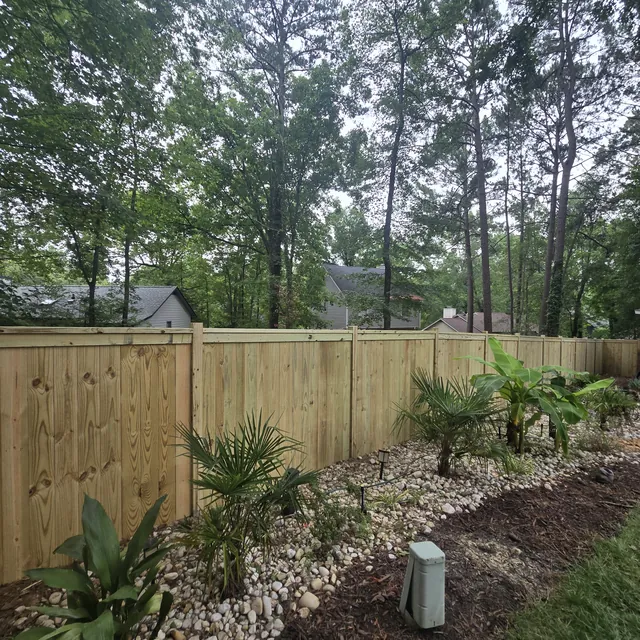 Pressure-treated wood privacy fence bordering a landscaped bed with river rock, installed by Superior Fence & Rail of Raleigh