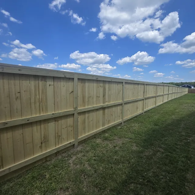 Pressure-treated wood privacy fence in a long straight run under open sky, installed by Superior Fence & Rail of Raleigh