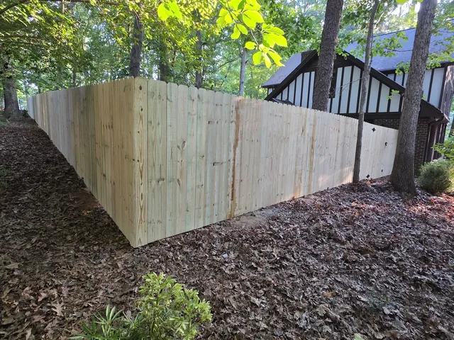 Pressure-treated wood privacy fence wrapping a wooded lot behind a Tudor-style home, installed by Superior Fence & Rail of Raleigh